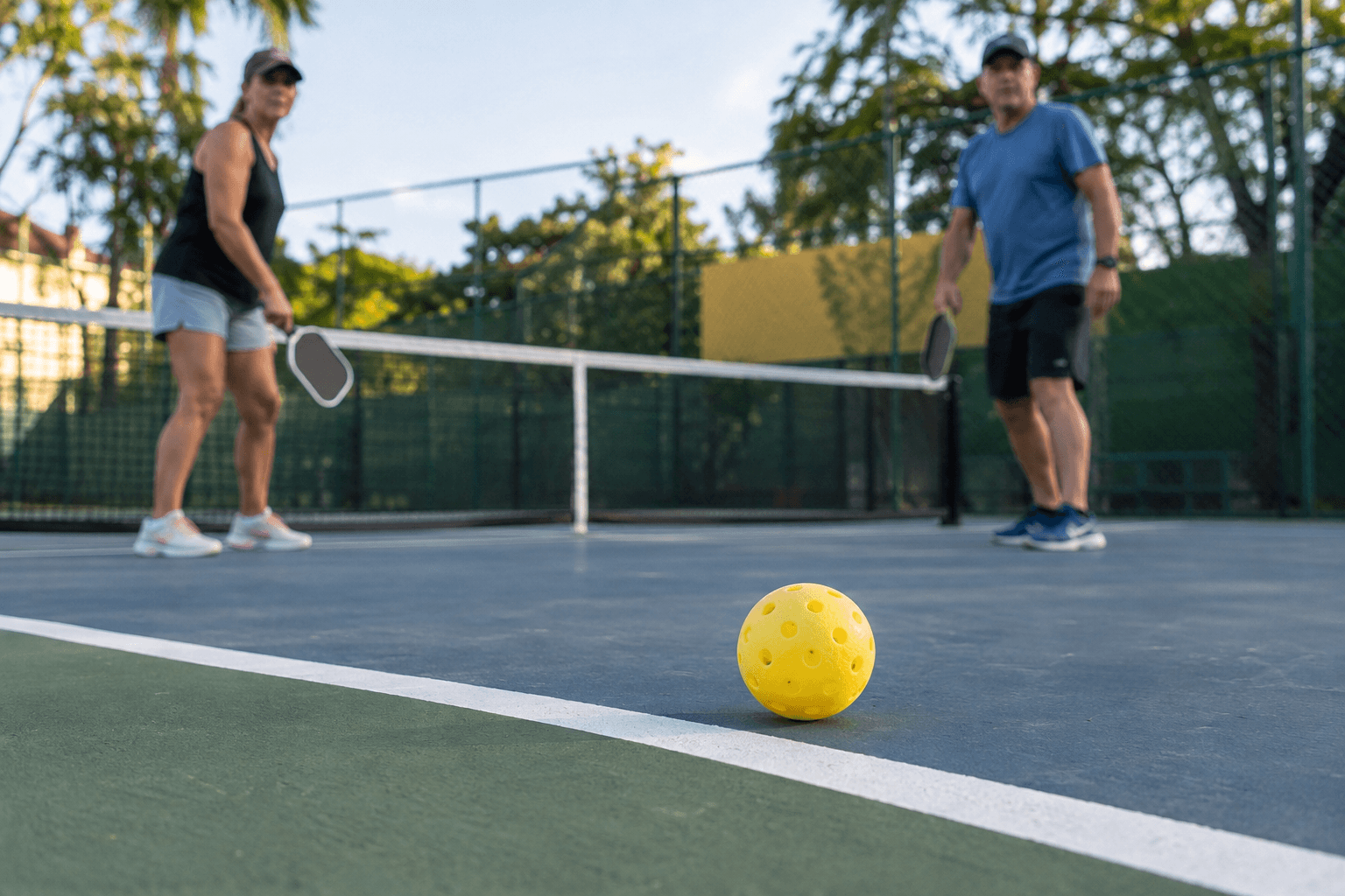 Jogadores em quadra recreativa de pickleball observam uma bola próxima à linha lateral